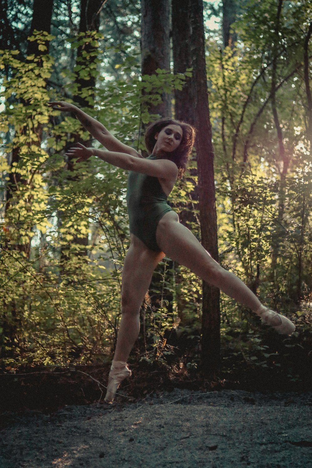 a woman in a green leotard is dancing in the woods