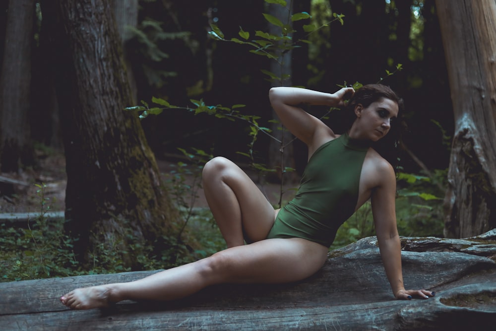 Una donna in un body verde seduta su una roccia nel bosco