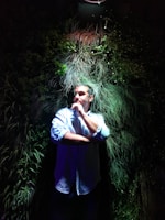 Portrait of a person with thoughtful expression against a dark green forest backdrop.