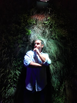 Portrait of a person with thoughtful expression against a dark green forest backdrop.