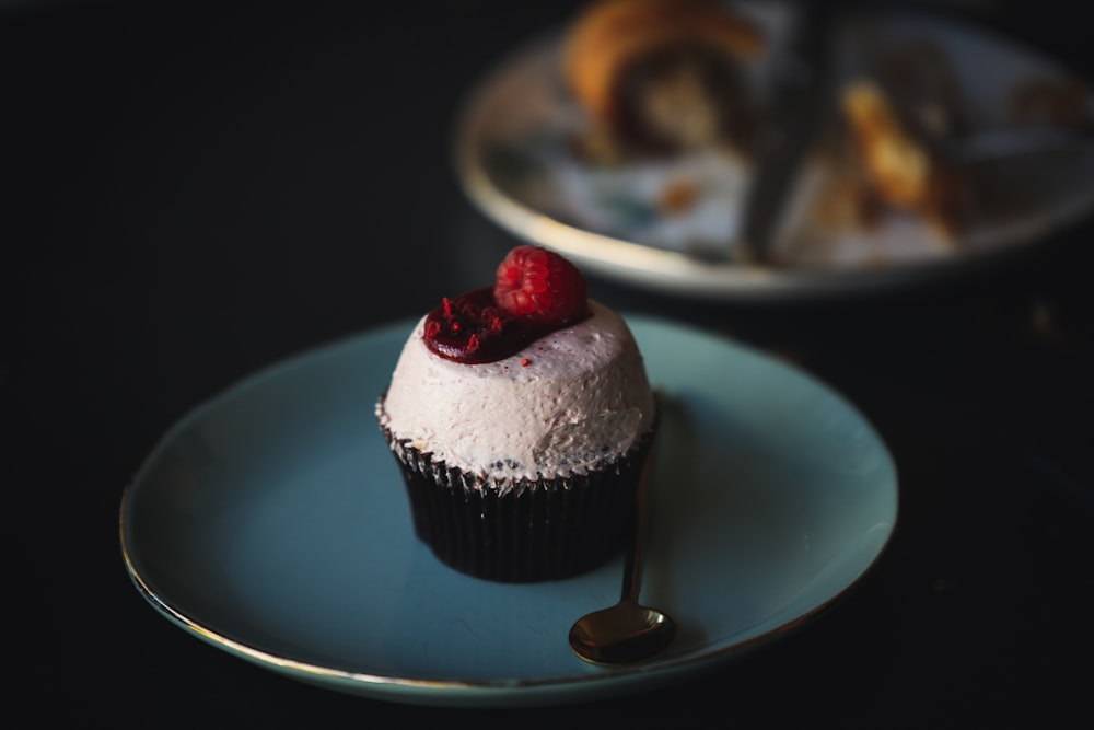 a cupcake with a raspberry on top on a plate