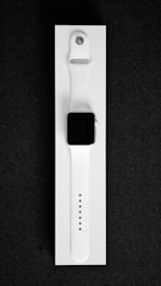 A white smartwatch with a rectangular black screen and a sleek, minimalist design is placed on a white background. The watch band is made of flexible material with multiple adjustment holes for sizing.