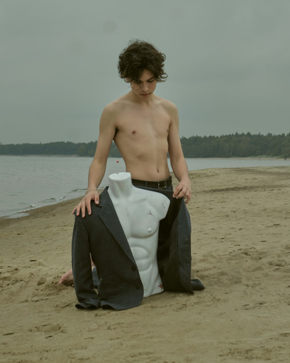 a shirtless man sitting on a beach next to a body of water