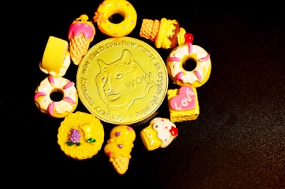 A gold coin featuring a dog meme design is surrounded by small, colorful toy desserts, including donuts, ice cream cones, and cakes, all set against a black background.