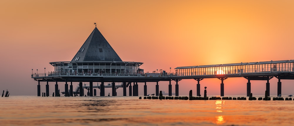 the sun is setting over a pier with a clock tower