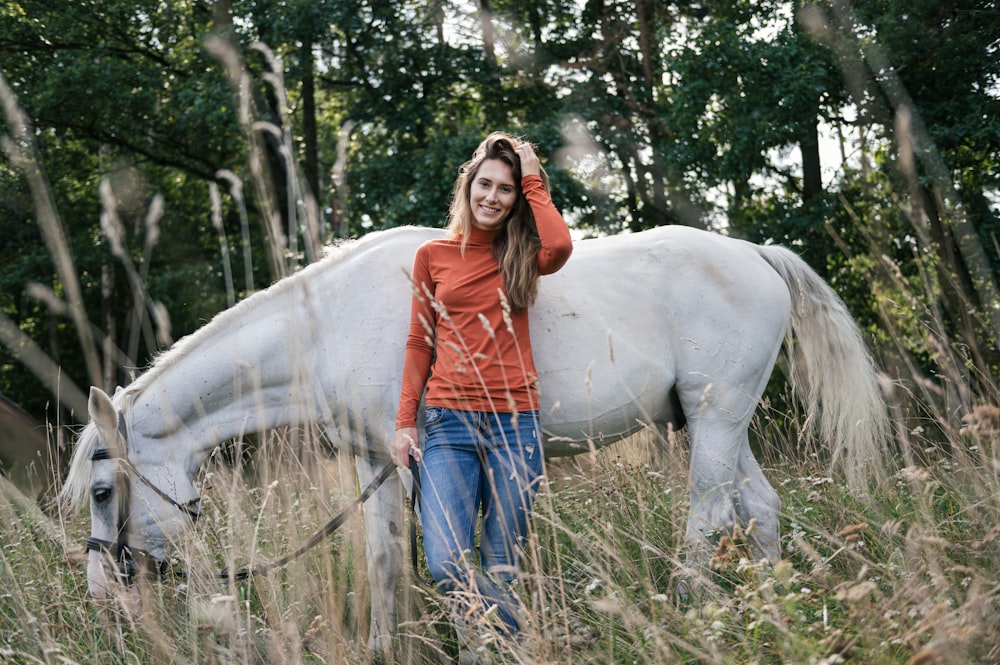 uma mulher que está ao lado de um cavalo branco em um campo