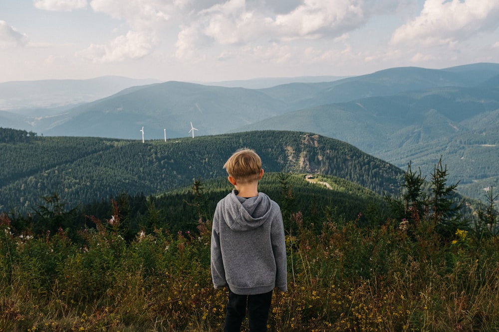 a young boy standing on top of a lush green hillside