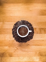 A steaming cup of blended coffee served on a wooden table with beans scattered around.