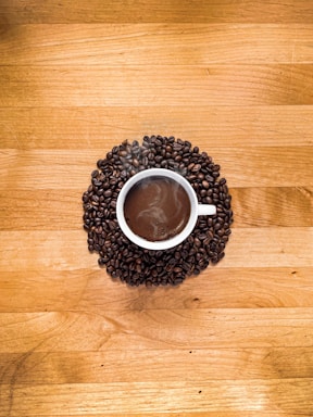 A warm cup of freshly brewed black coffee on a wooden table with coffee beans scattered around.