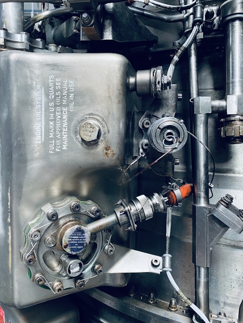 A detailed view of an industrial mechanical system, featuring metallic components such as pipes, valves, and bolts arranged in a complex structure. The surface of the metal parts is marked with technical inscriptions and a few spots of rust. Wires and connectors run alongside the metal parts, suggesting functionality related to machinery or engineering.