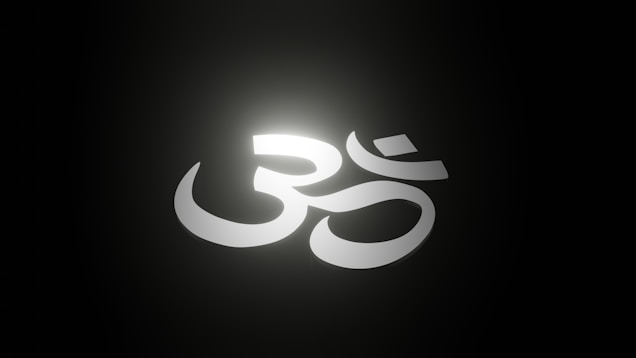 A white Om symbol is illuminated against a dark background, creating a glowing effect with a soft halo of light around it.