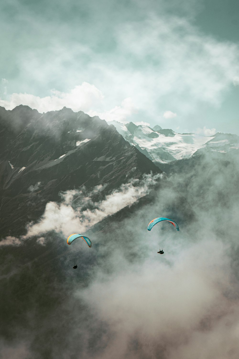 two paragliders are flying over a mountain range