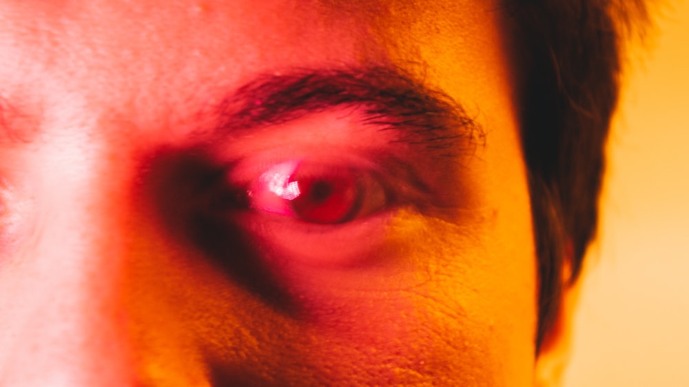 un gros plan de l’œil d’un homme avec une lumière rouge dessus