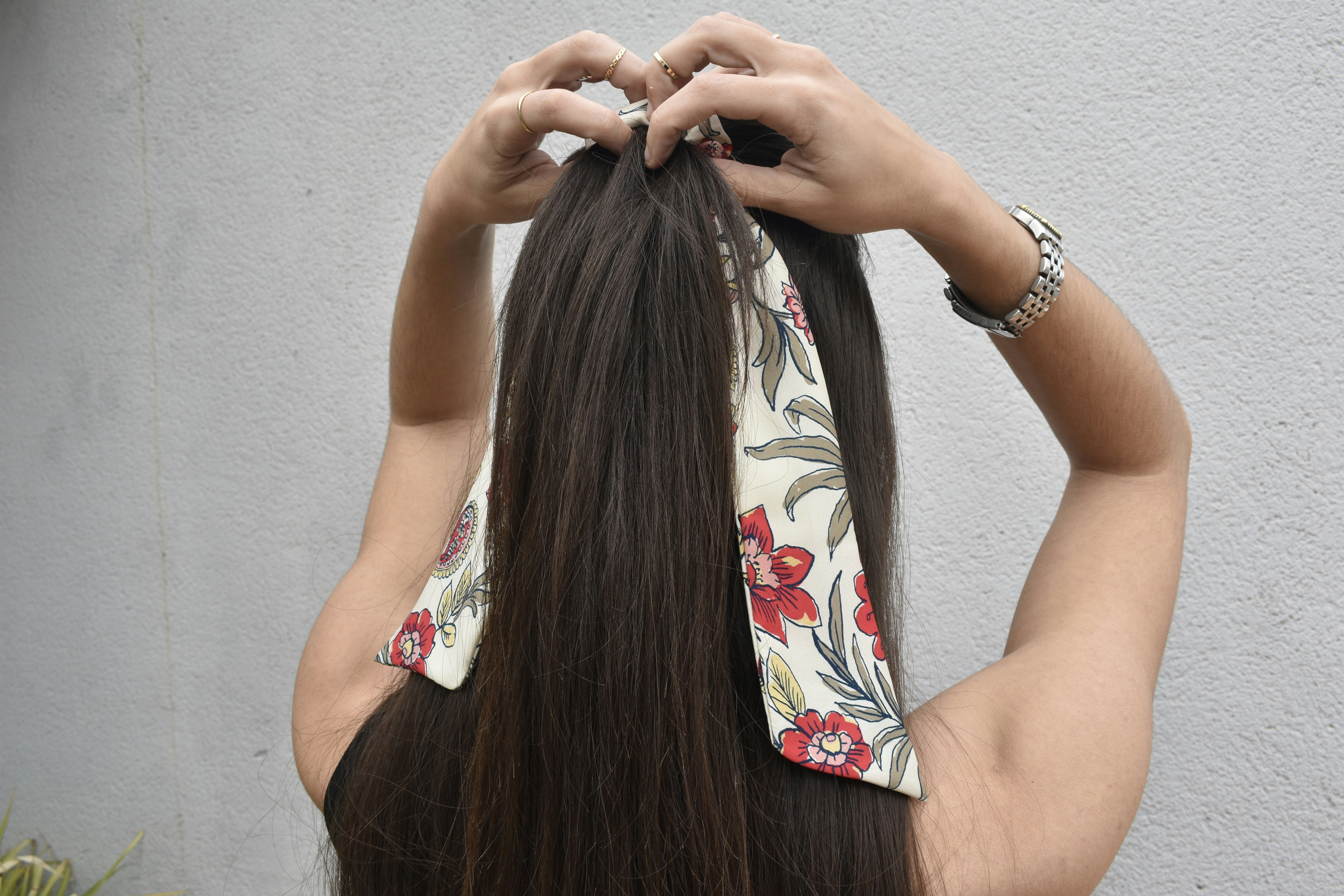 Woman tying floral scarf over long straight dark brown clip-in hair extensions.