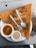 A large triangular dosa is placed on a white plate, accompanied by two small bowls of sauces, one orange and one cream-colored. A fork and spoon are resting on top of the dosa.