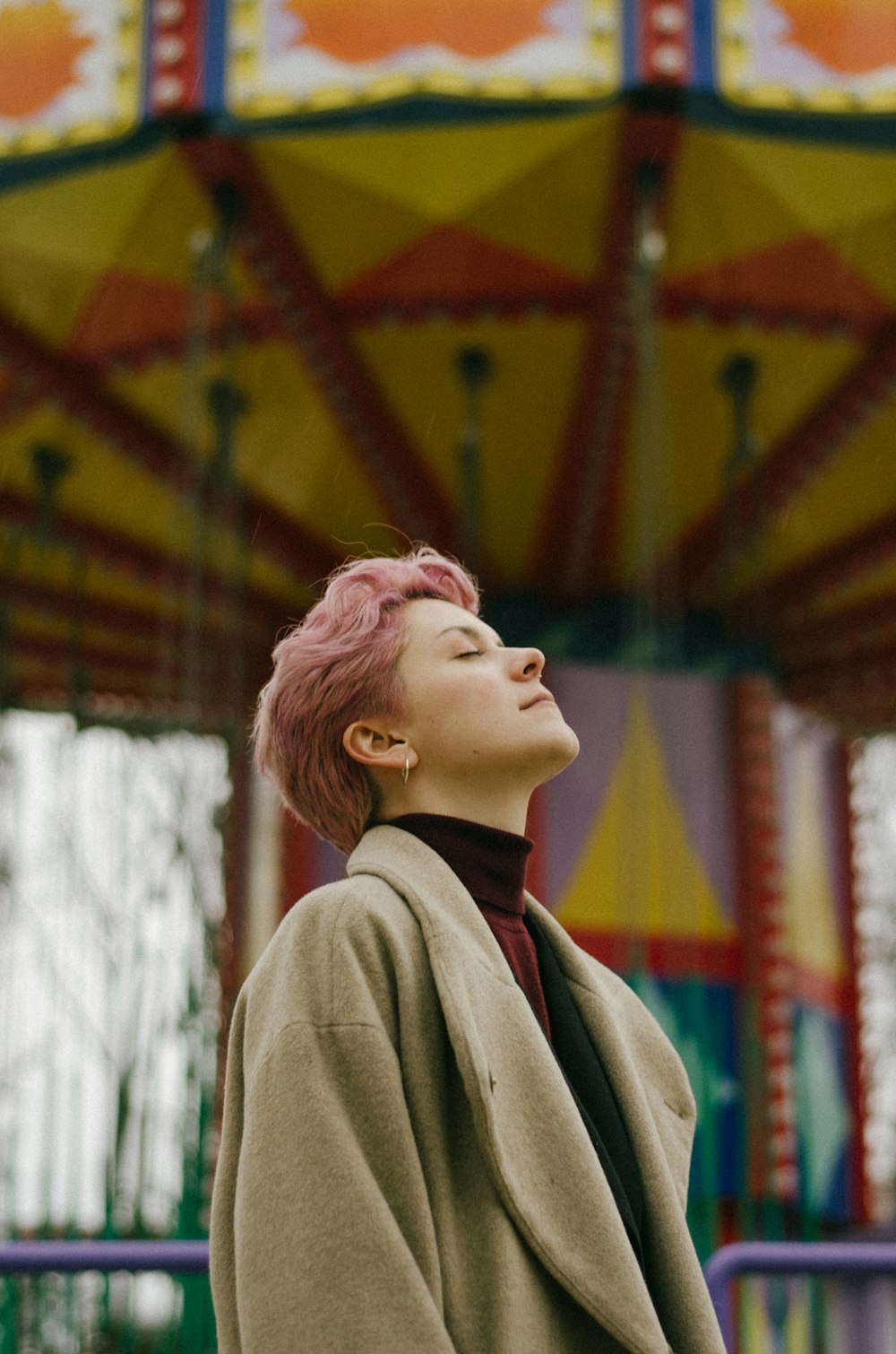 a woman with pink hair standing in front of a carousel