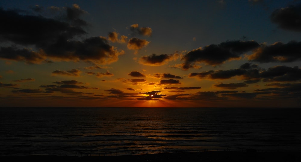 the sun is setting over the ocean on a cloudy day