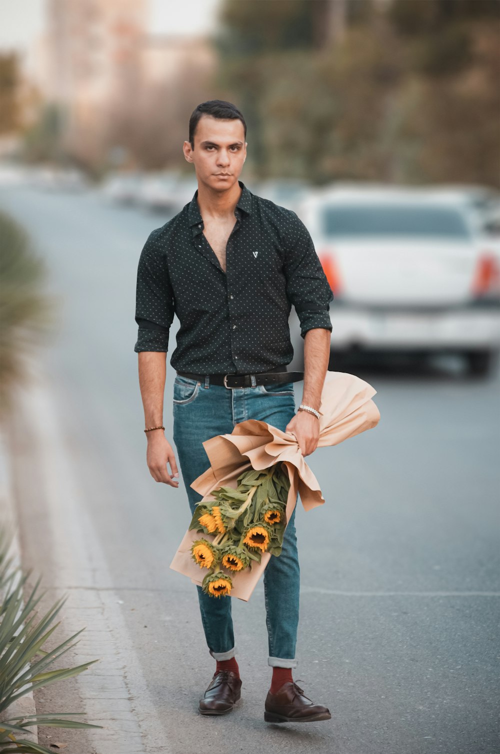 a man holding a bunch of sunflowers on the side of a road