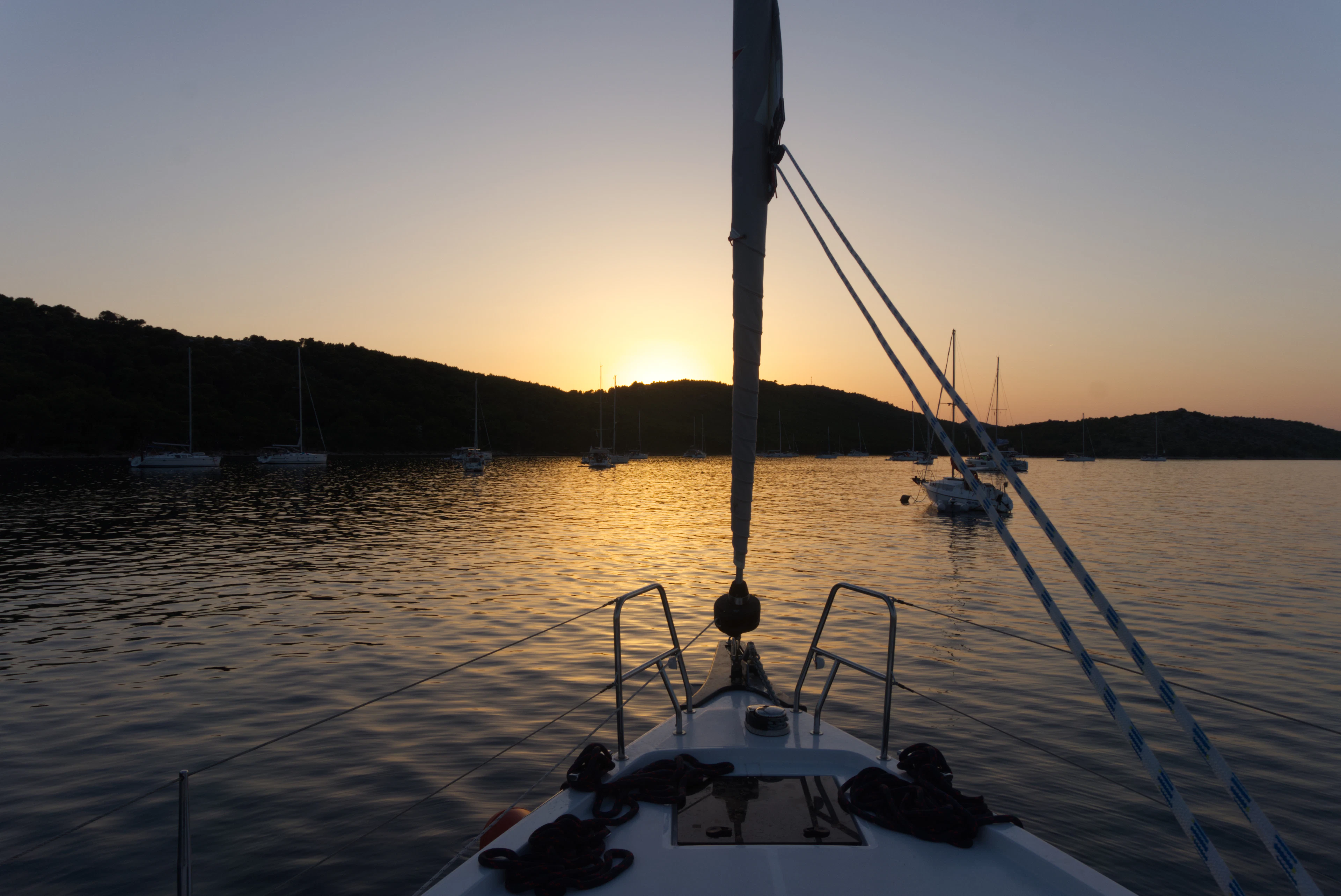 Sunset seen from the bow of a sailing yacht in a calm Kornati bay, with other boats at anchor