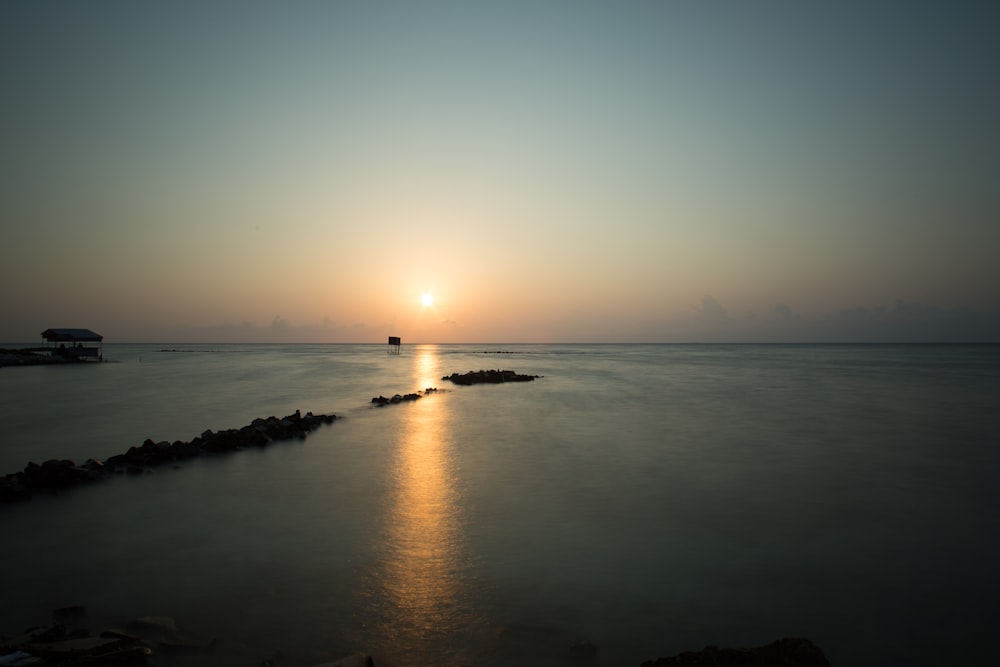 the sun is setting over the ocean with rocks in the foreground