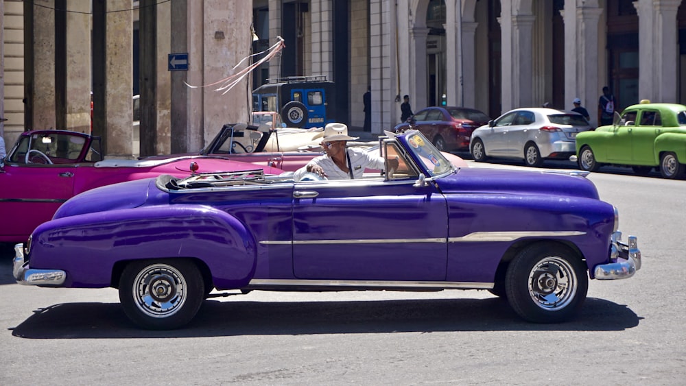 Un coche morado conduciendo por una calle junto a edificios altos