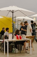 a group of people sitting at a table under umbrellas