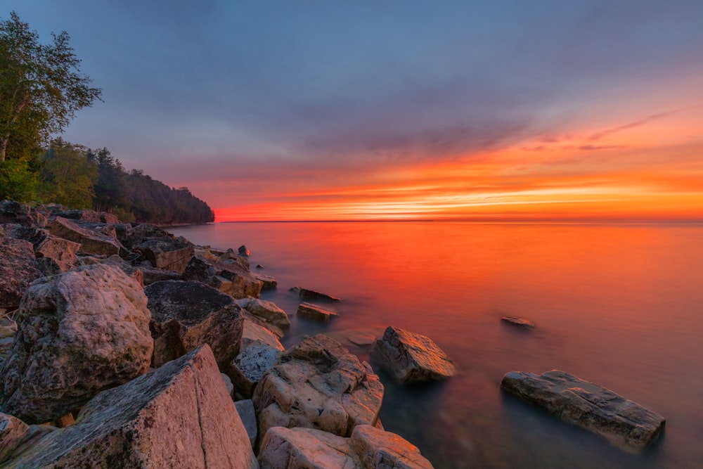a beautiful sunset over the ocean with rocks in the foreground