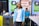 A person with long braided hair is wearing a light blue blazer over a white shirt and dark pants. They are standing in front of a background that includes branding for Beauty Point College. There is a seated audience and tables with bottled drinks in the background.