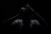 a man in the dark covering his face with his hands