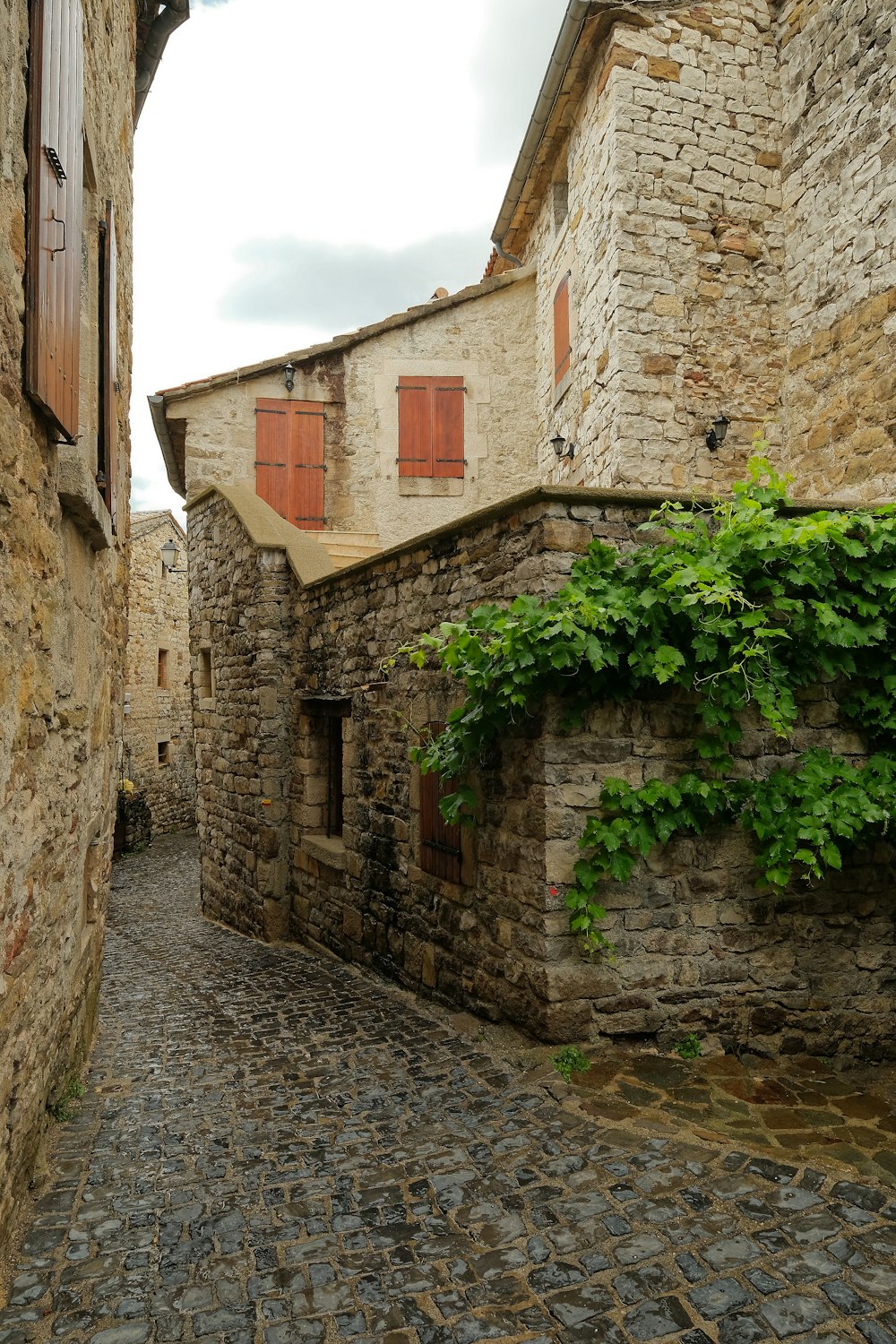 Una calle empedrada con un edificio de piedra con persianas rojas
