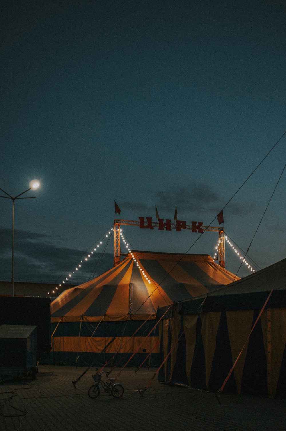 a circus tent lit up at night with a bicycle parked in front of it