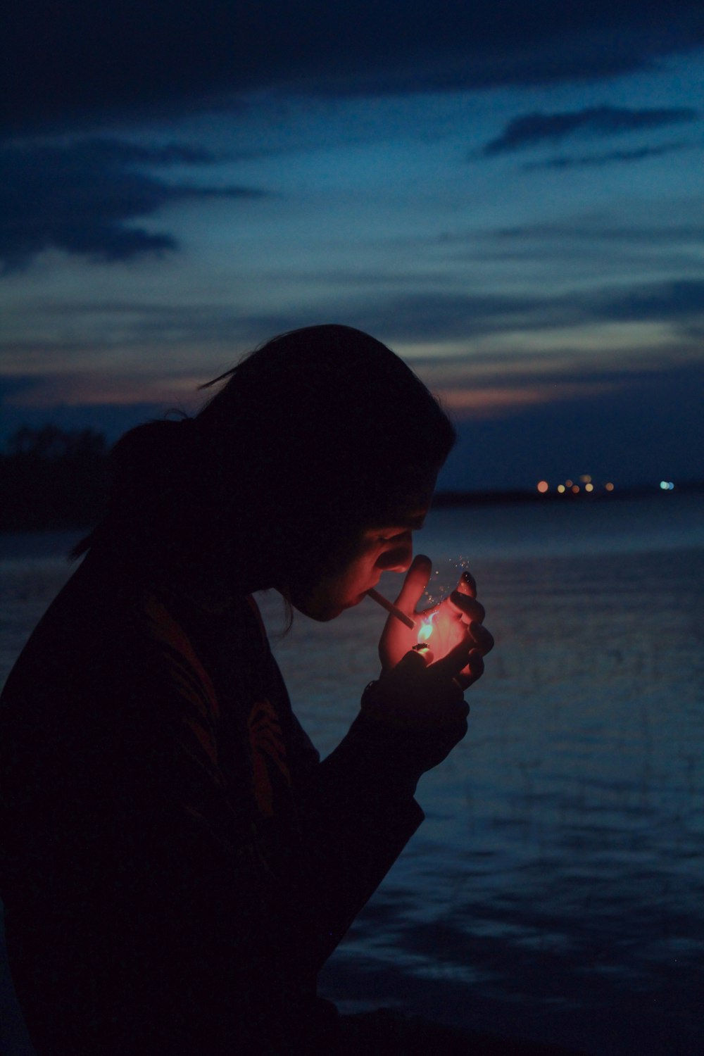 a woman holding a lit candle in front of a body of water