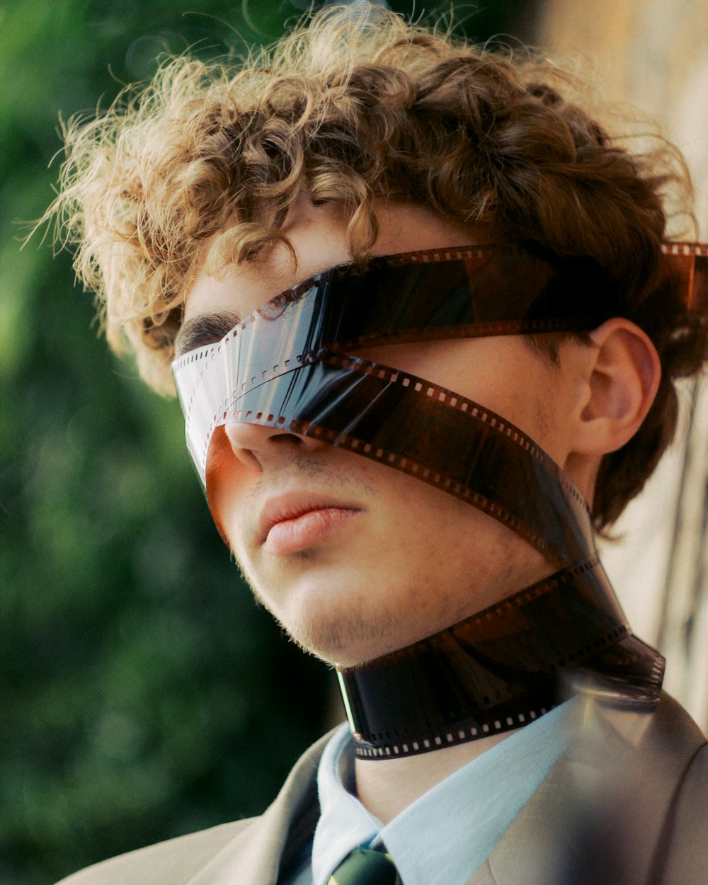 a man wearing a tie and blindfold with trees in the background