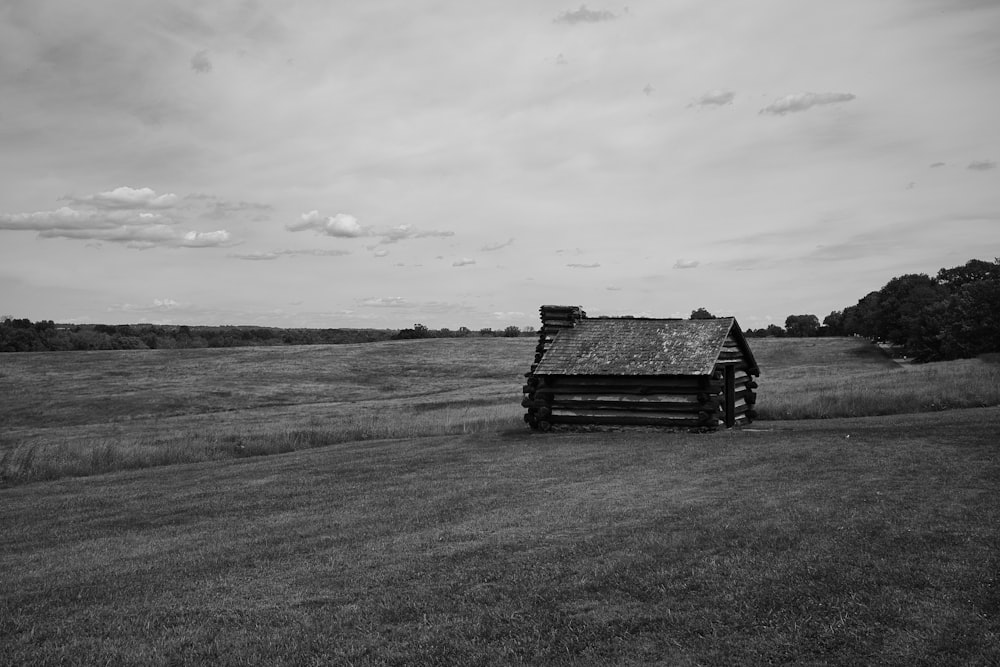 a black and white photo of a log cabin in a field