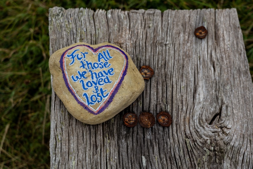 Un caillou sur lequel est écrit "For all those we have loved and lost" entouré d'un coeur de couleur
