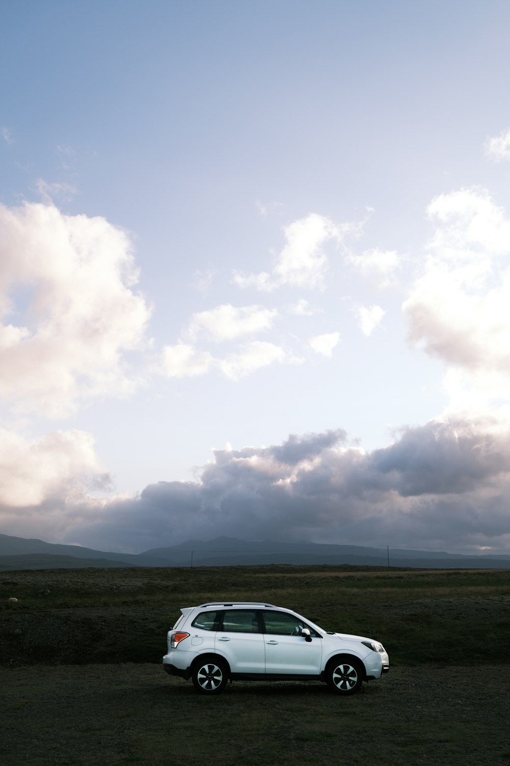 a white car parked in a field under a cloudy sky