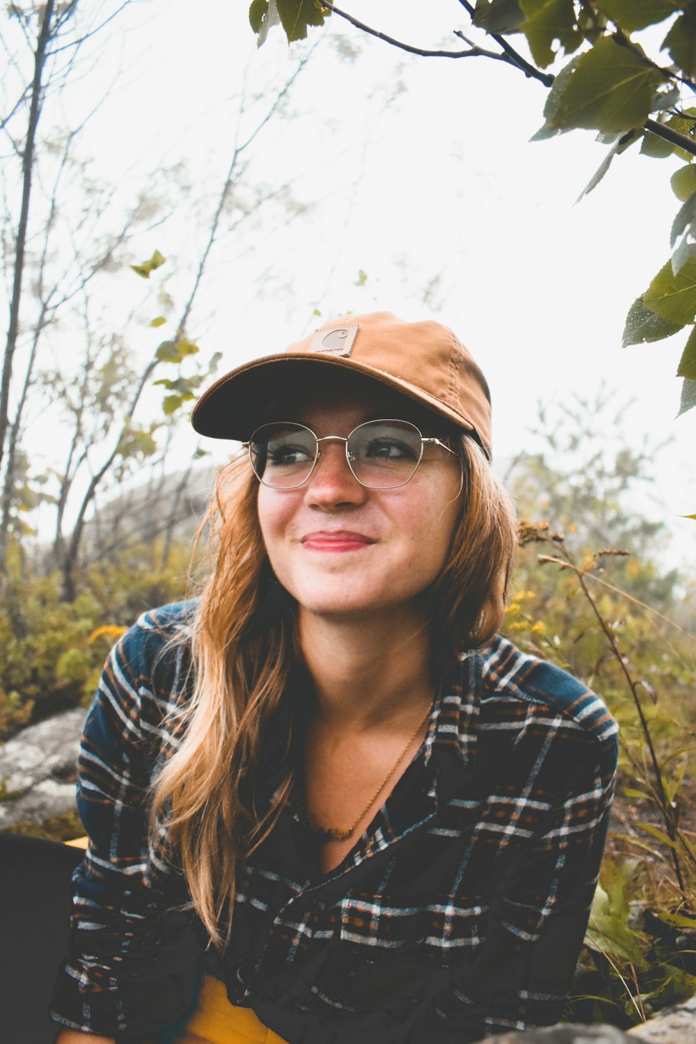 a woman wearing a hat and glasses sitting on a rock