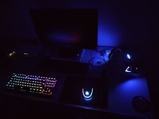 a desk with a keyboard, mouse and monitor lit up in the dark