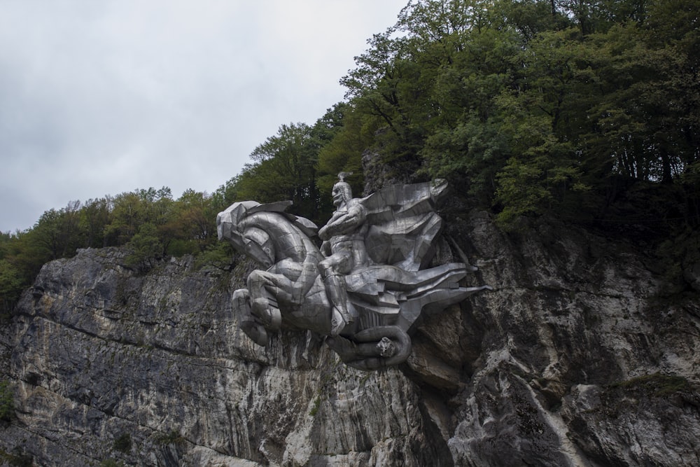 a statue of a woman riding a horse on top of a cliff