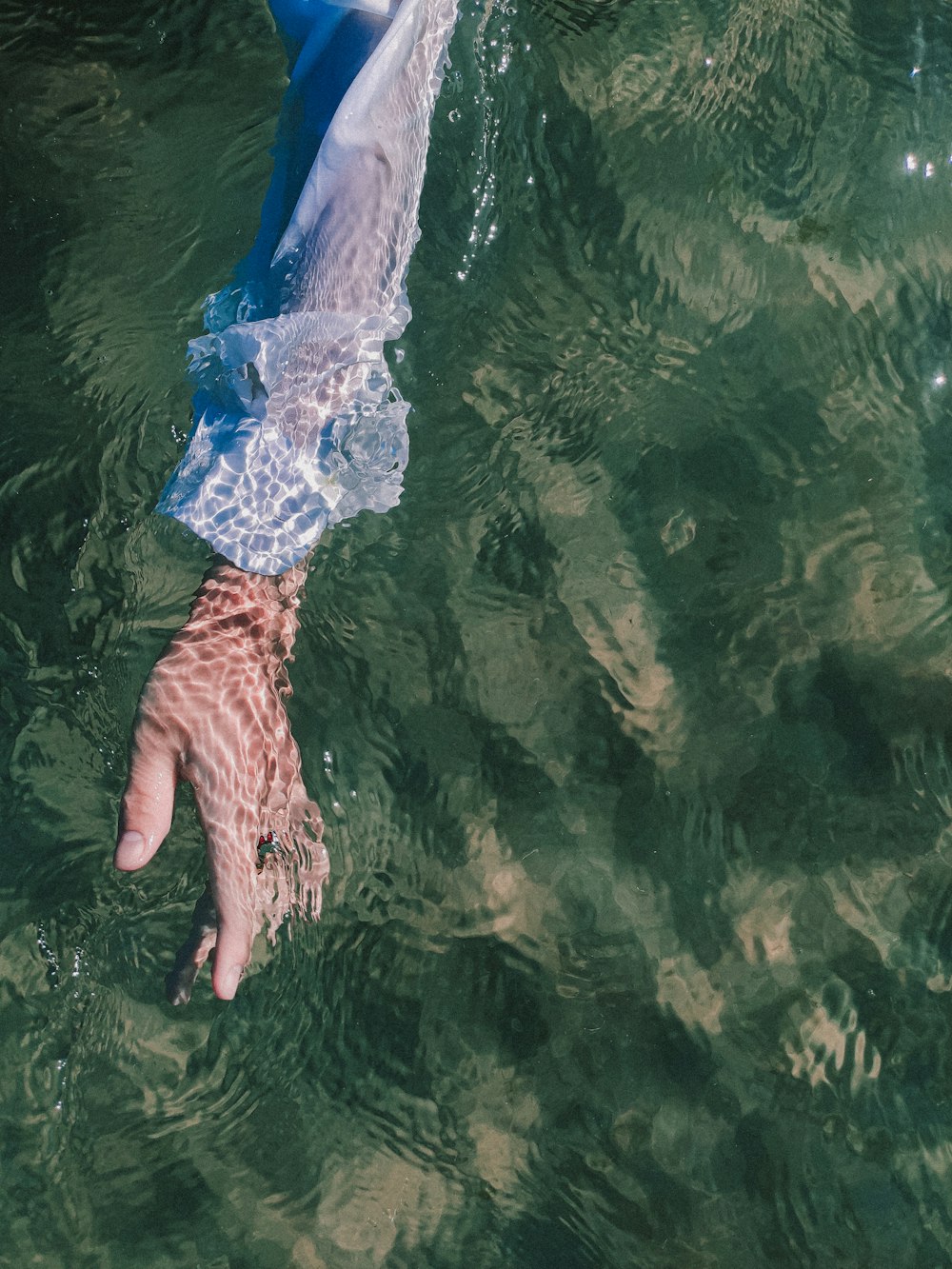 a person's hand reaching for a frisbee in the water