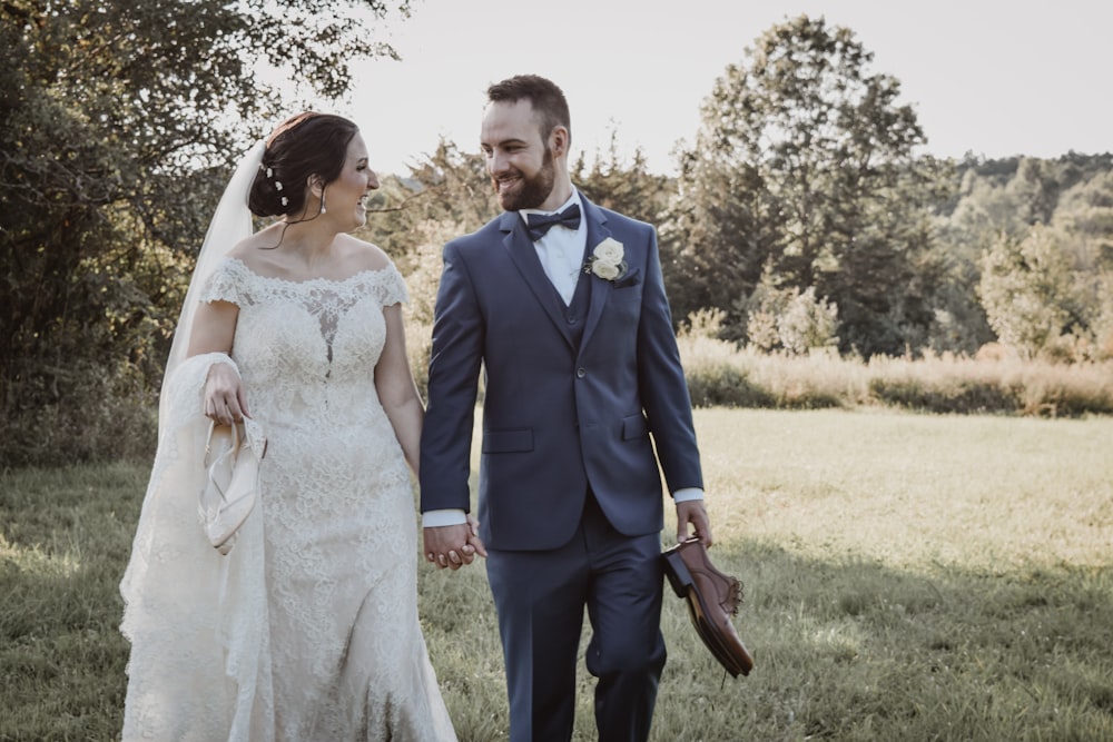 a bride and groom walking through a field