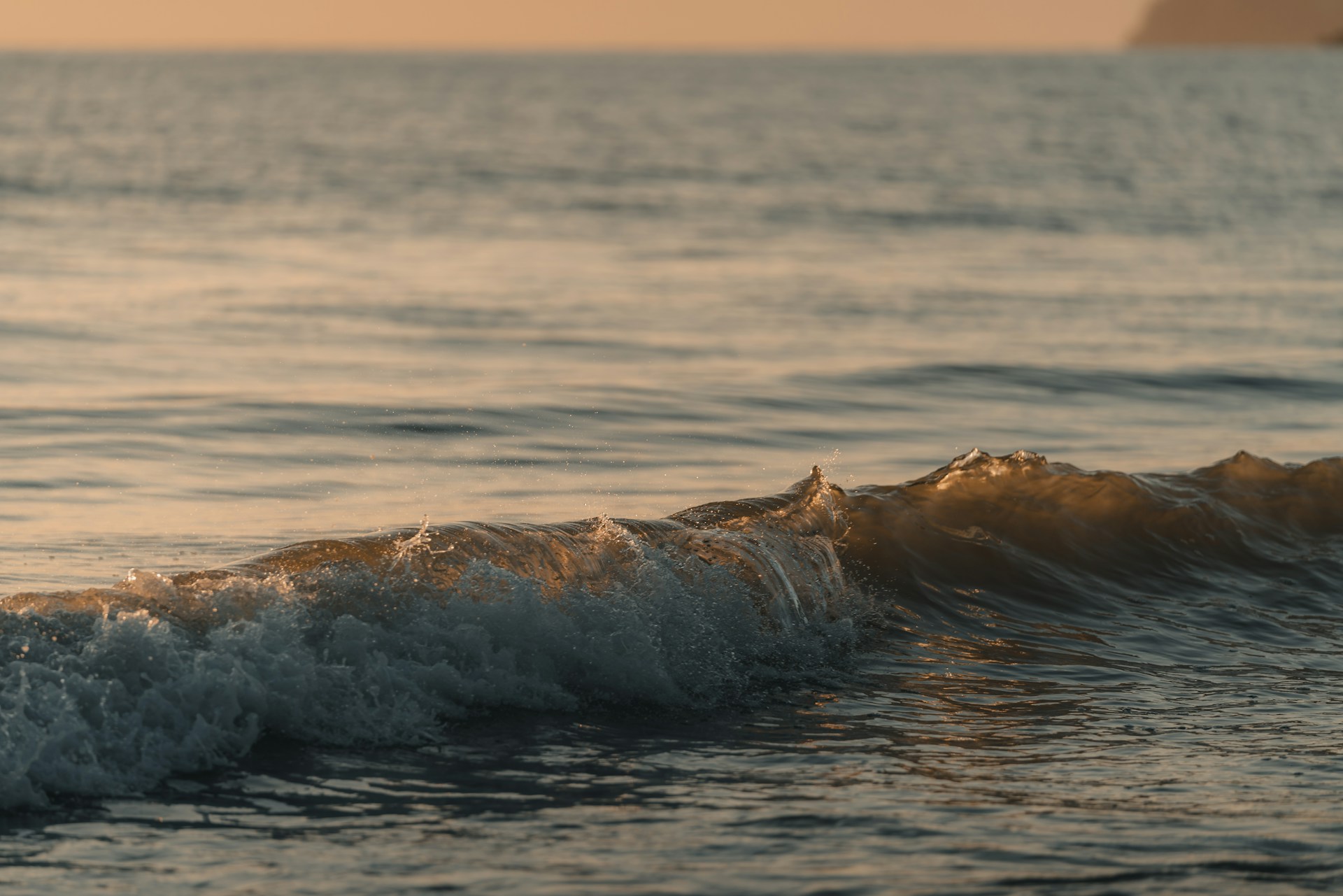 A gentle slide revealing a calm ocean wave rolling onto a sandy beach at sunset.