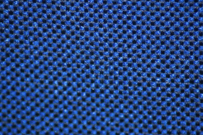 A close-up view of a textured surface composed of a grid pattern with small, raised bumps. The surface is predominantly blue and has a fabric-like appearance, suggesting it could be a piece of material or upholstery.