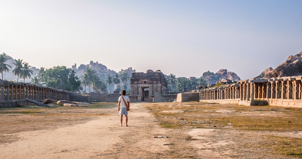 a man standing on a dirt road in front of a building