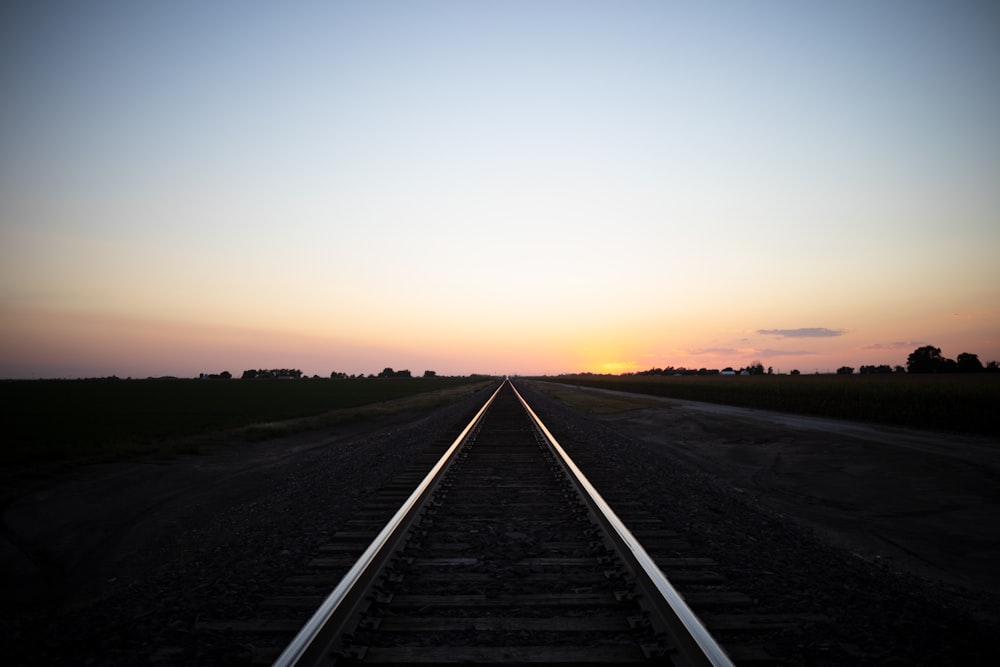 uma linha de trem com o pôr do sol à distância