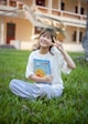 a young girl sitting in the grass holding a book