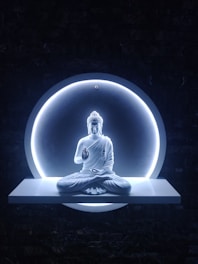 A serene white statue of Buddha is seated in a meditative pose, set against a dark background. The statue is illuminated by a circular halo of light, which creates a glowing effect around the figure. The platform beneath the statue is sleek and minimalistic, enhancing the overall tranquility of the scene.