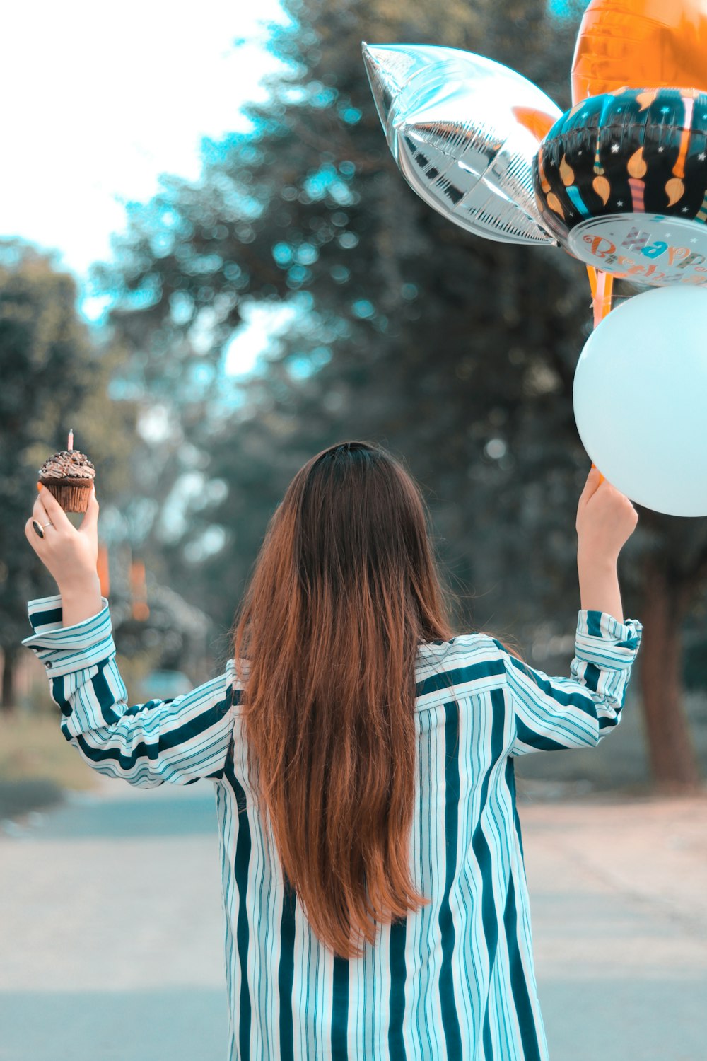 Una mujer sosteniendo una magdalena frente a un montón de globos