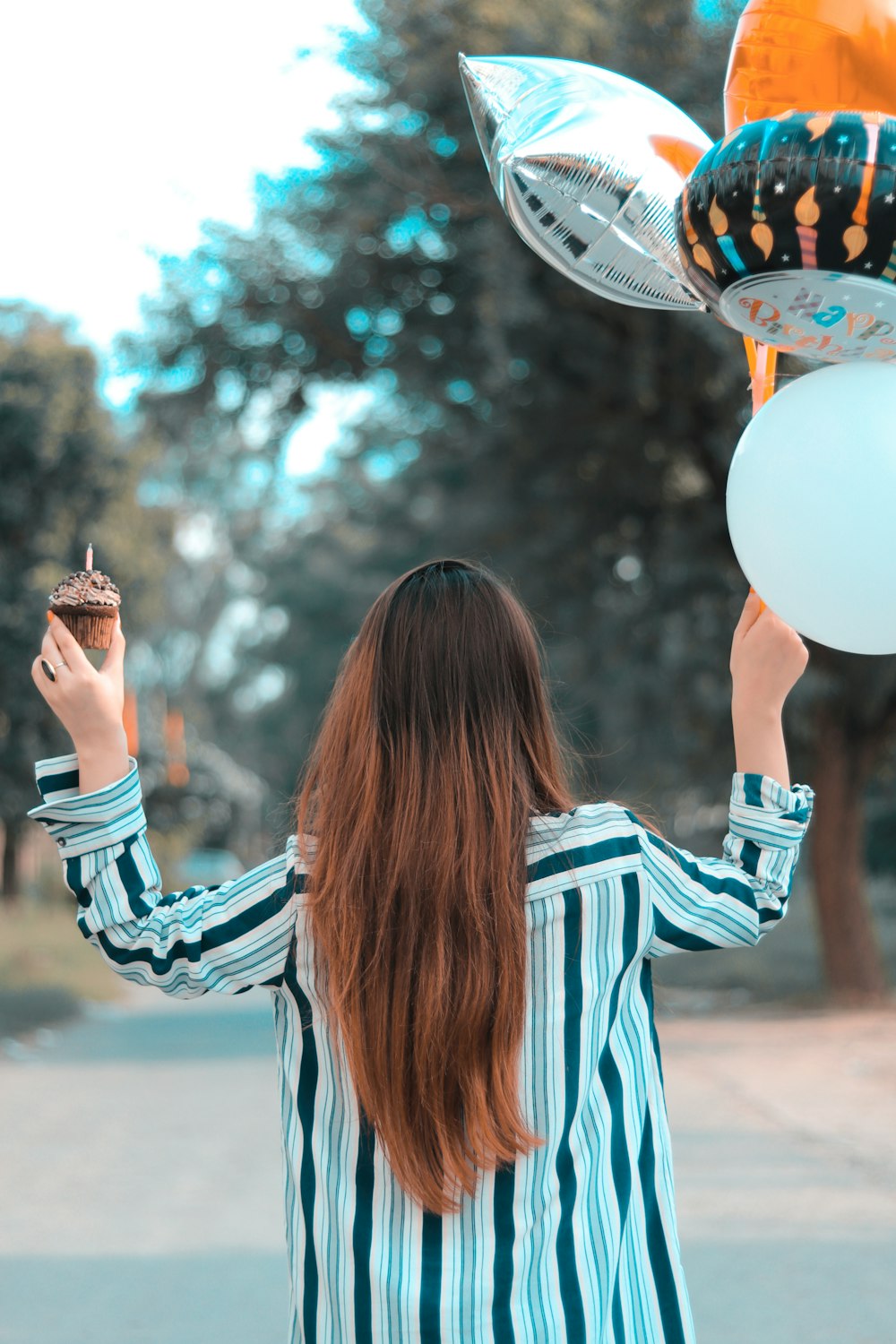 a woman holding a cupcake in front of a bunch of balloons