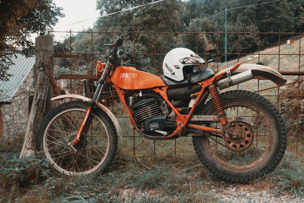 an orange dirt bike parked next to a fence